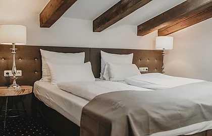 Gemütliches Doppelbett in Hotelzimmer mit Holzbalken, moderner Beleuchtung und stilvollem Nachttisch