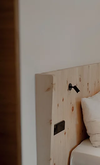 Nahaufnahme eines hochwertigen Bettes in schlichtem Design mit hellem Holz-Kopfteil, weißen Kissen und Leselampen