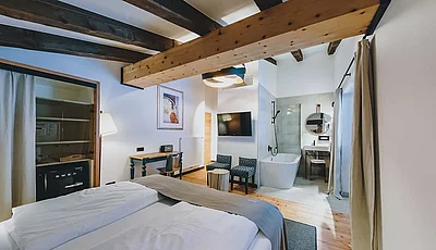 Stilvolles Hotelzimmer mit Holzbalken, freistehender Badewanne, Doppelbett und moderner Einrichtung