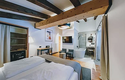 Stilvolles Hotelzimmer mit Holzbalken, freistehender Badewanne, Doppelbett und moderner Einrichtung