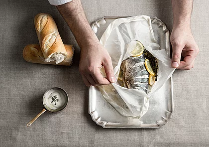 In Backpapier gegarter Fisch mit Zitronenscheiben und Kräutern, serviert mit Weißbrot und Sauce