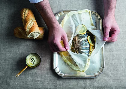In Backpapier gegarter Fisch mit Zitronenscheiben und Kräutern, serviert mit Weißbrot und Sauce