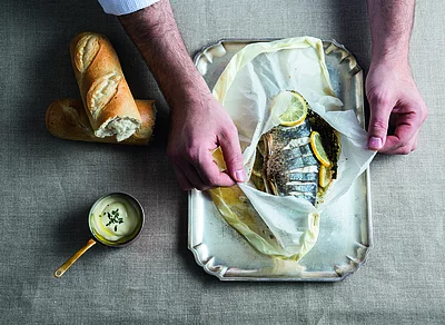 In Backpapier gegarter Fisch mit Zitronenscheiben und Kräutern, serviert mit Weißbrot und Sauce