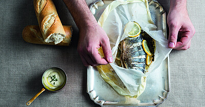 In Backpapier gegarter Fisch mit Zitronenscheiben und Kräutern, serviert mit Weißbrot und Sauce