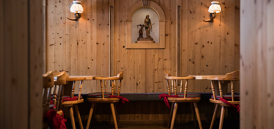 Our restaurant Traditionelle Holzstube mit geschnitzter Wandverzierung, Holzstühlen und stimmungsvoller Beleuchtung