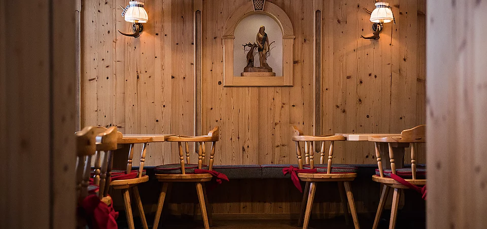 Our restaurant Traditionelle Holzstube mit geschnitzter Wandverzierung, Holzstühlen und stimmungsvoller Beleuchtung