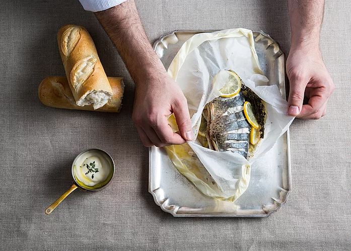 In Backpapier gegarter Fisch mit Zitronenscheiben und Kräutern, serviert mit Weißbrot und Sauce
