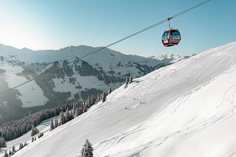 Skifahrer auf verschneiter Piste unter roter Gondel im Skigebiet Saalbach Hinterglemm Leogang Fieberbrunn