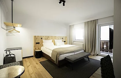 Modernes Hotelzimmer mit Doppelbett, hellem Holzdesign, Sitzbank, Teppich, Balkon und stilvollen Vorhängen