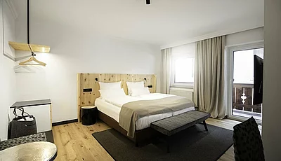 Modernes Hotelzimmer mit Doppelbett, hellem Holzdesign, Sitzbank, Teppich, Balkon und stilvollen Vorhängen