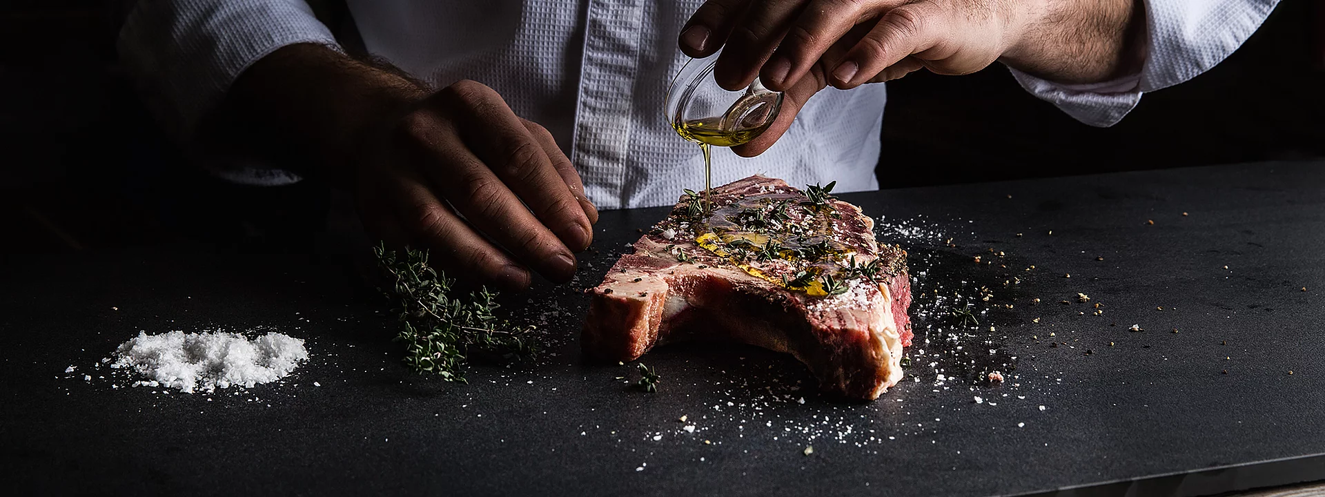 Ein Koch mariniert rohes Steak mit Olivenöl, Kräutern, Gewürzen und Meersalz