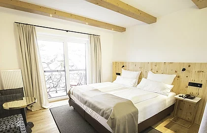 Helles Hotelzimmer mit Doppelbett, Holzbalken, Balkon, Vorhängen und stilvollen Sitzmöbeln